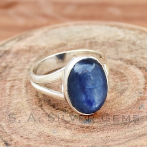 May include: A silver ring with a blue oval gemstone. The ring has a split band design.