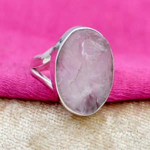 May include: A silver ring featuring a large, round, opaque, pale pink gemstone. The gemstone has a rough, textured surface.