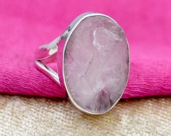 May include: A silver ring with a large, round, opaque, light pink gemstone. The gemstone has a rough, textured surface.