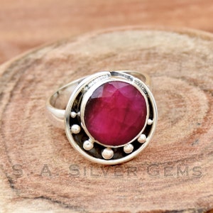 Peut inclure: Une bague en argent avec une grande pierre précieuse en rubis rose facetté sertie dans une bélière circulaire. La bélière est ornée d'un motif décoratif de petites boules d'argent autour du bord.