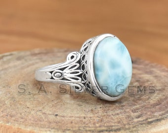 May include: A silver ring with a blue and white oval gemstone. The ring has a detailed filigree design.