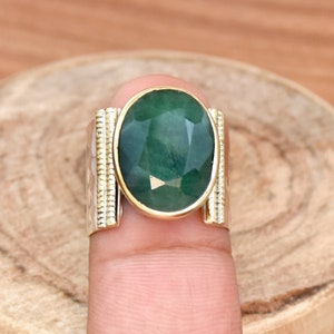 May include: A silver ring with a green oval gemstone set in gold. The ring has a textured band.