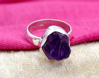 May include: A silver ring with a large, faceted amethyst gemstone. The amethyst is a deep purple color and has a rough, natural look.