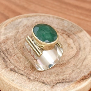 May include: A silver and gold ring with a large green oval gemstone. The ring has a textured band and a gold setting for the stone.