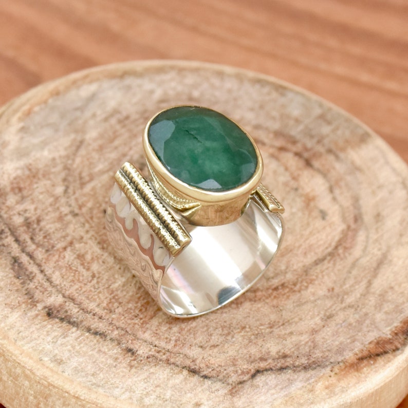May include: A silver and gold ring with a large green oval gemstone. The ring has a textured band and a gold setting for the stone.