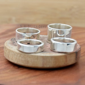 May include: Four silver rings of varying sizes are displayed on a wooden surface. The rings are all smooth and polished, with a slightly rounded edge. The rings are arranged in a semi-circle, with the largest ring at the top and the smallest ring at the bottom. The text "S.A. SILVER GEMS" is visible in the background.