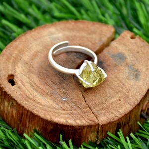 May include: A silver ring featuring a raw, light green gemstone. The ring is displayed on a wooden surface.