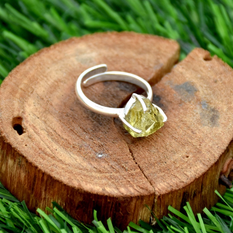May include: A silver ring featuring a raw, light green gemstone. The ring is displayed on a wooden surface.