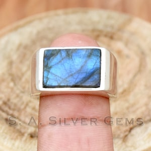 May include: A silver ring featuring a rectangular blue labradorite gemstone. The ring is worn on a finger.