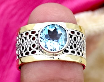 Könnte beinhalten: Ein Silber- und Goldring mit einem blauen Topas-Edelstein. Der Ring hat ein dekoratives, durchbrochenes Design.