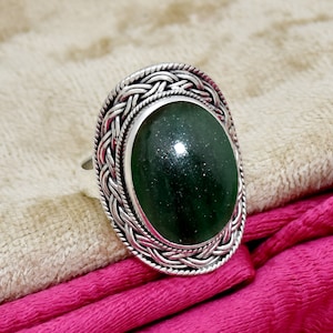 May include: A silver ring with a green oval gemstone set in a braided design.