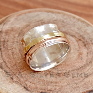 Può includere: Un anello girevole in argento, oro e oro rosa. L'anello è composto da tre bande che ruotano l'una intorno all'altra.