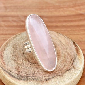 Op de afbeelding: Een zilveren ring met een grote ovale rozenkwarts edelsteen. De ring heeft een eenvoudige band en de steen is gezet in een bezel setting.