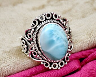 May include: A silver ring with a blue and white oval gemstone set in a decorative silver setting. The ring has a detailed design with swirls and beads.