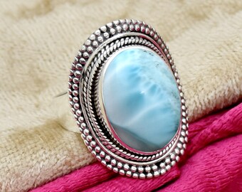 May include: A silver ring with a blue and white oval cabochon gemstone set in a detailed silver bezel. The ring has a textured band and a decorative border around the stone.