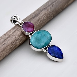 Op de afbeelding: Een zilveren hanger met drie edelstenen: een ronde rode robijn, een ovale groene smaragd en een traanvormige blauwe saffier.