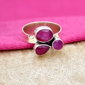 May include: A silver ring with three pink ruby stones. The stones are set in a cluster and are surrounded by a silver band.