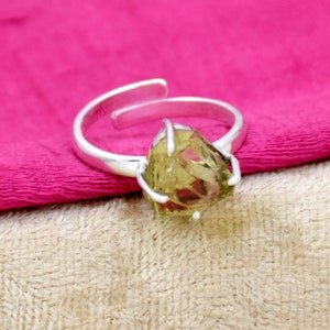 May include: A silver ring featuring a large, faceted, green gemstone. The gemstone is set in a silver claw setting.