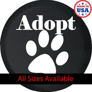 May include: Black spare tire cover featuring a white paw print and the word "Adopt" in white. The cover also includes the text "All Sizes Available" and a "Made in USA" emblem.