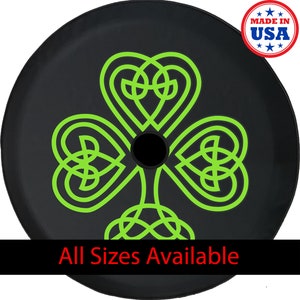 May include: Black tire cover featuring a neon green Celtic knot shamrock design. The cover has a central black hole and the text "All Sizes Available" at the bottom. A "Made in USA" sticker is in the upper right corner.