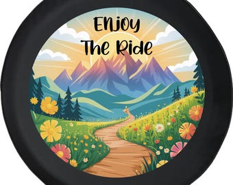 May include: Black spare tire cover with a colorful landscape design. The image features a path winding through a field of wildflowers, leading to mountains under a sunset. Text at the top reads "Enjoy The Ride."