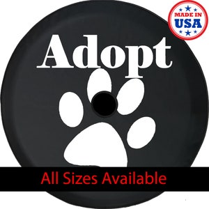 May include: Black spare tire cover with the word "Adopt" in white, along with a white paw print. The cover also has the text "All Sizes Available" and a "Made in USA" emblem.