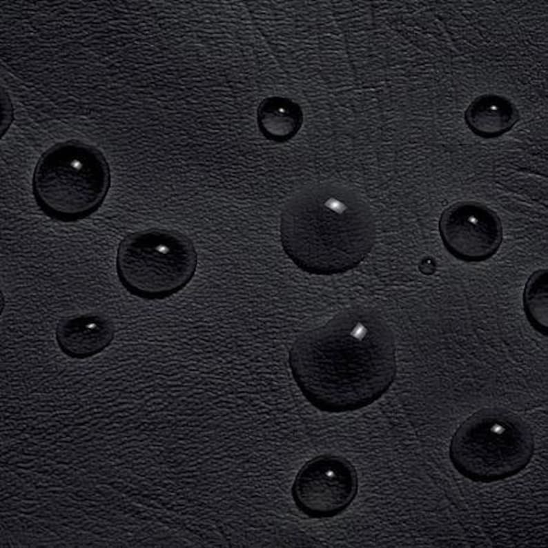 May include: Close-up of a black, textured surface with several large, clear water droplets. The droplets reflect light, creating bright highlights against the dark background. The surface appears to be leather or a similar material.