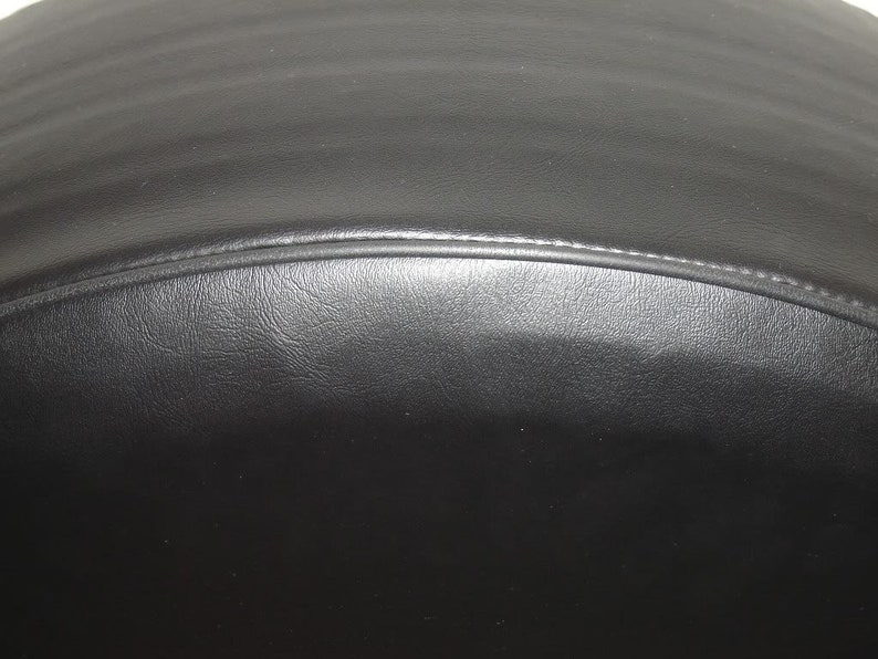 May include: Close-up of a black leather object with a curved shape. The leather has a textured surface and a stitched seam along the curved edge. The object appears to be a part of a larger item.