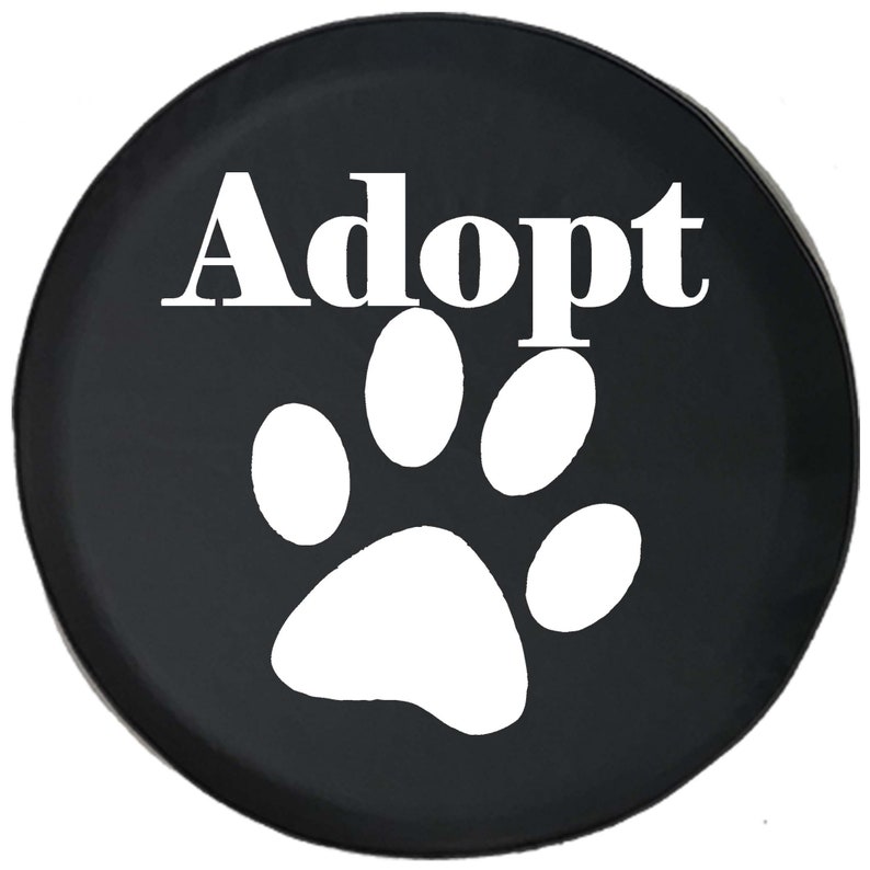 May include: A black circular cover featuring the word "Adopt" in white, above a white paw print. The cover is likely for a spare tire or similar item, promoting pet adoption.