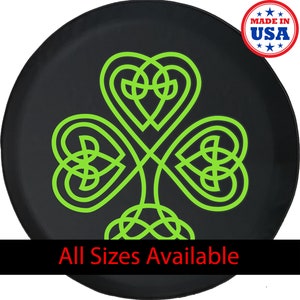 May include: Black tire cover featuring a neon green Celtic knot shamrock design. The shamrock is a three-leaf clover, a symbol of Ireland. The text "All Sizes Available" is at the bottom. A "Made in USA" sticker is in the upper right corner.