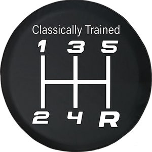 May include: Black spare tire cover featuring a white graphic of a manual transmission gear shift pattern with the numbers 1, 2, 3, 4, 5, and R. The text "Classically Trained" is above the gear shift pattern.