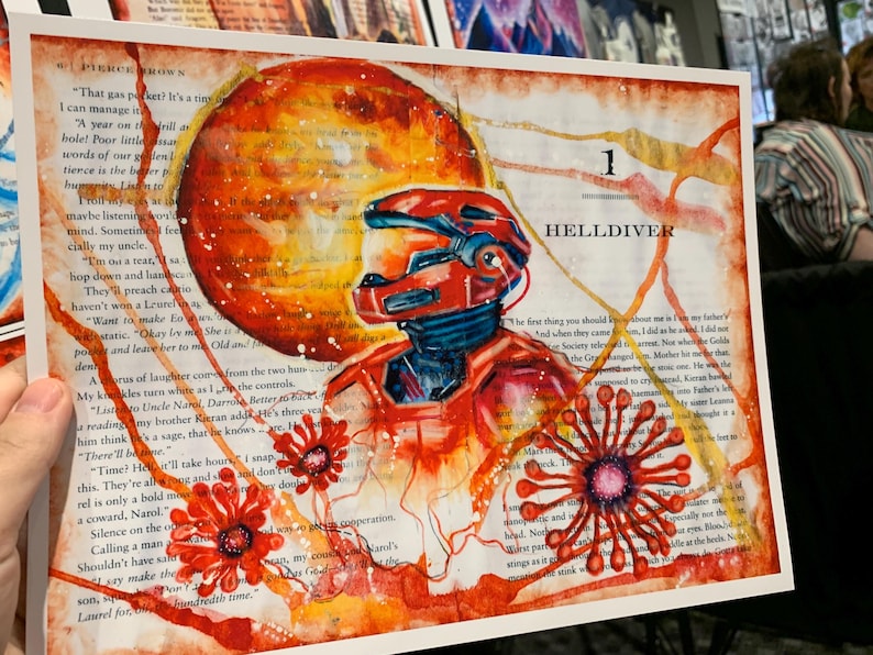 May include: A rectangular art print featuring a red armored figure in a helmet, set against a background of printed book text. A large orange sphere sits behind the figure, with red floral-like shapes and orange paint splatters throughout.