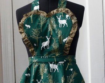 May include: A green apron with a heart-shaped neckline and gold trim. The apron features a white deer and forest print.