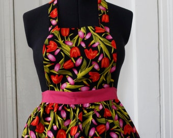 May include: A black apron with a pink waistband and a tulip print in shades of red, pink, and green.