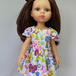 May include: A doll with long brown hair wearing a white dress with a colourful floral and butterfly print.