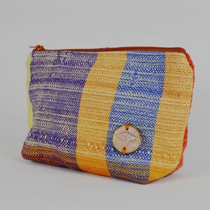 May include: A colourful striped zippered pouch with a brown leather zipper pull and a ceramic button with a design. The pouch is made of woven fabric and has a yellow, orange, blue, and purple striped pattern.