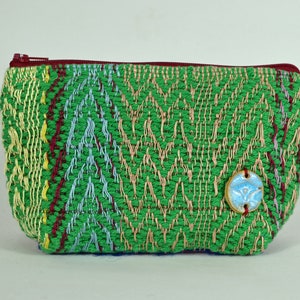 May include: A green zippered pouch with a woven pattern and a blue and white ceramic button. The pouch has a red zipper and a variety of colours in the woven pattern.