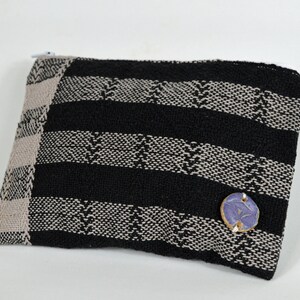 May include: A black and beige striped fabric pouch with a zipper closure and a small blue ceramic button.