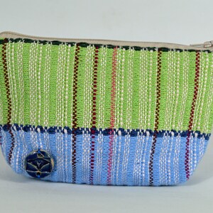 May include: A green and blue woven zippered pouch with a blue button. The pouch has a striped pattern.