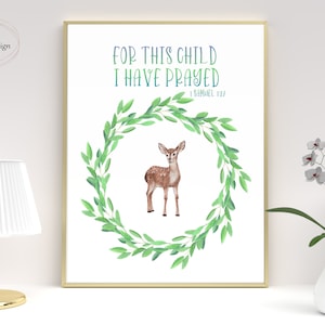 Può includere: Una stampa ad acquerello con una ghirlanda di foglie verdi e un cervo marrone al suo interno. Il testo recita "Per questo bambino ho pregato" con il riferimento biblico "1 Samuele 1:27".