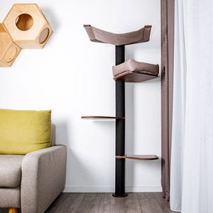 Peut inclure: Un arbre à chat moderne avec un poteau central noir et plusieurs plateformes. Il comprend un lit en forme de hamac, un lit carré et deux étagères en bois. L'arbre à chat est placé contre un mur blanc, avec une maison pour chat en bois et un canapé.