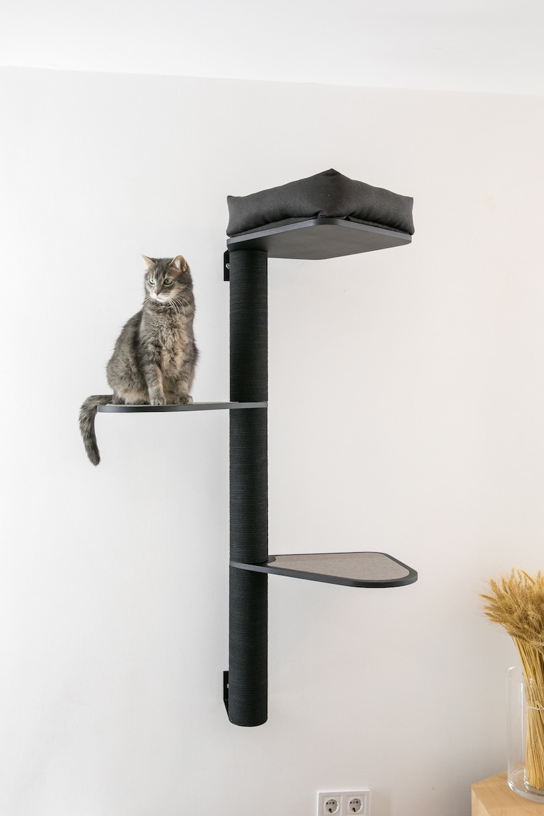 May include: A black cat tree with three platforms and a bed. The cat tree is mounted to a white wall. The cat tree is made of wood and has a black fabric covering. The cat tree is 7 feet tall.