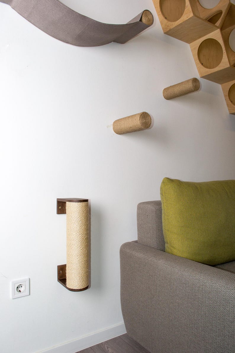 Pode incluir: Um poste de arranhar para gatos de madeira marrom com corda de sisal enrolada ao redor est&aacute; montado em uma parede branca. O poste est&aacute; ao lado de um sof&aacute; cinza com uma almofada verde.