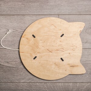 May include: A light wood cat scratching post with a rope attached. The scratching post is shaped like a cat's head with ears.
