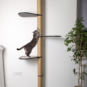 Puede incluir: Un &aacute;rbol para gatos alto de color beige con un poste para rascar de sisal y varias plataformas negras. Un gato gris est&aacute; trepando por el poste para rascar. El &aacute;rbol para gatos est&aacute; en una habitaci&oacute;n con paredes blancas y suelo gris. Hay una planta en maceta en la esquina de la habitaci&oacute;n.