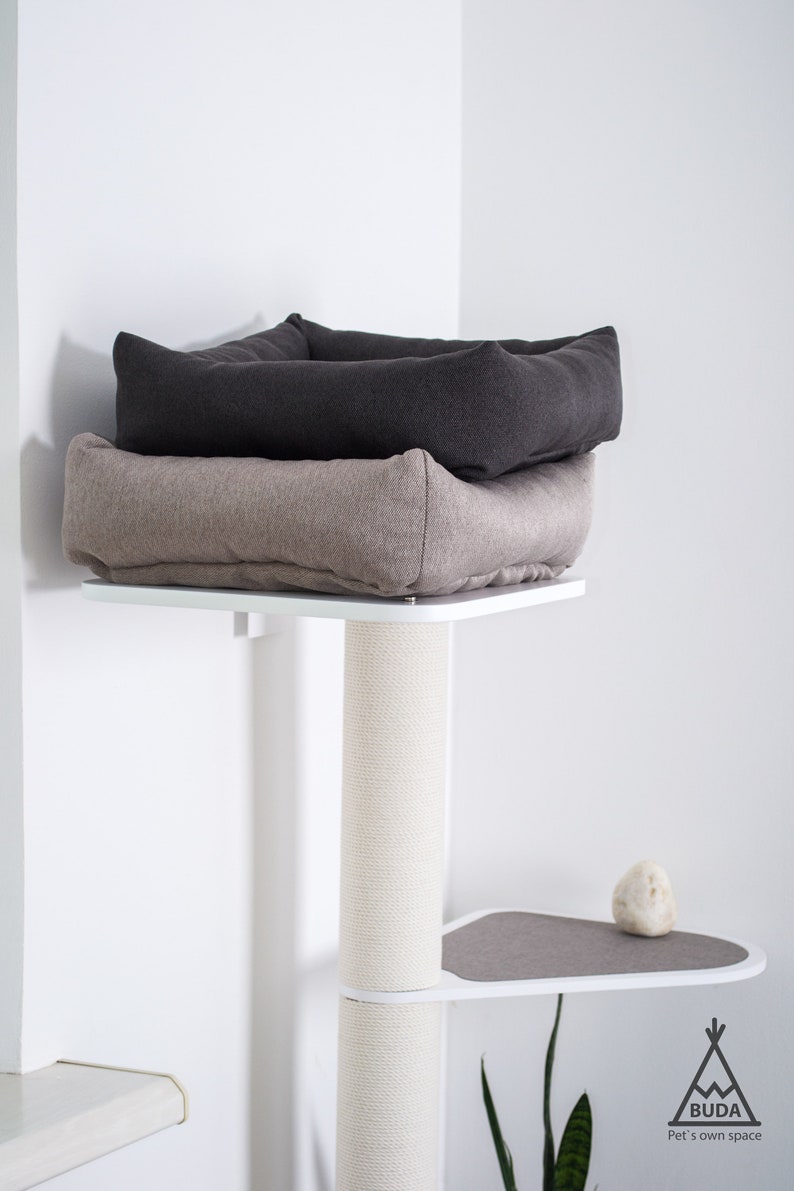 May include: A white cat tree with a beige and gray cat bed on top. The cat tree has a sisal-covered scratching post and a gray platform.