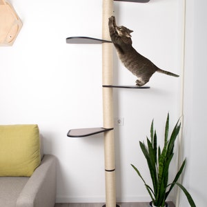 Puede incluir: Un &aacute;rbol para gatos alto de color beige con una plataforma negra y un poste para rascar de sisal. Un gato atigrado est&aacute; subiendo por el poste. El &aacute;rbol para gatos est&aacute; en una habitaci&oacute;n con un sof&aacute; y una planta.