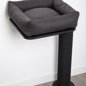 May include: A gray cat bed with a black base and a scratching post. The bed is mounted to the wall and has a soft, cushioned interior.