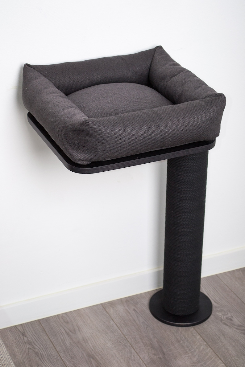 May include: A gray cat bed with a black base and a scratching post. The bed is mounted to the wall and has a soft, cushioned interior.