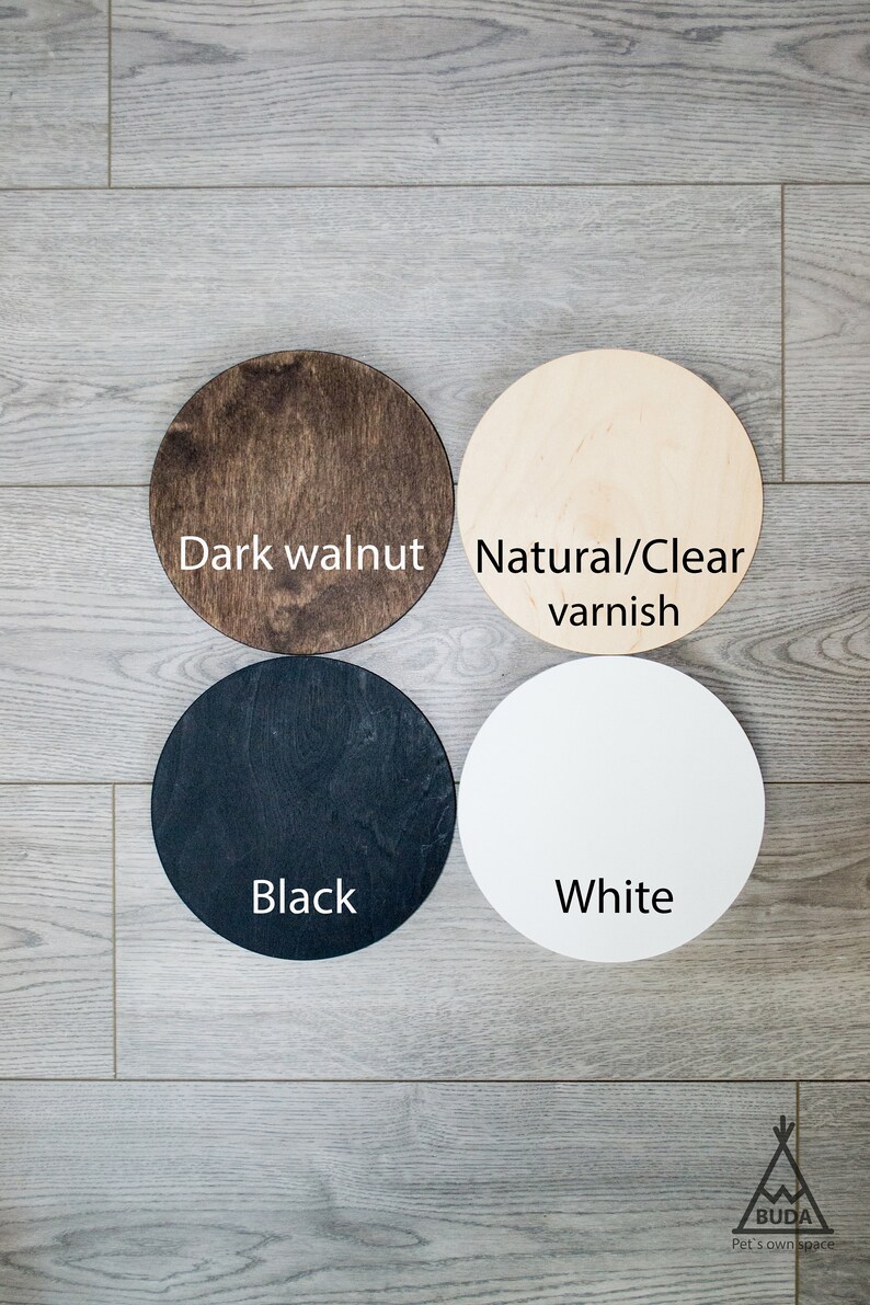 May include: Four wooden circles in different colors: dark walnut, natural/clear varnish, black, and white. The circles are arranged in a square pattern on a woodgrain surface.